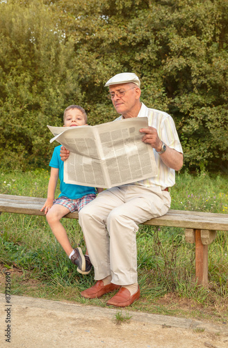Senior man and bored child reading newspaper outdoors