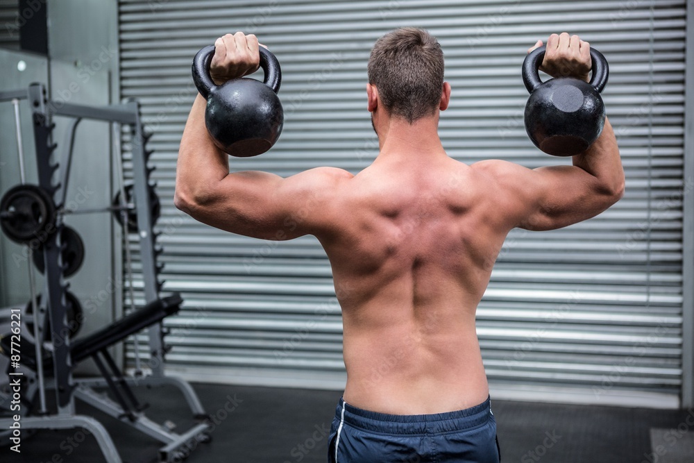 Muscular man lifting two kettlebells