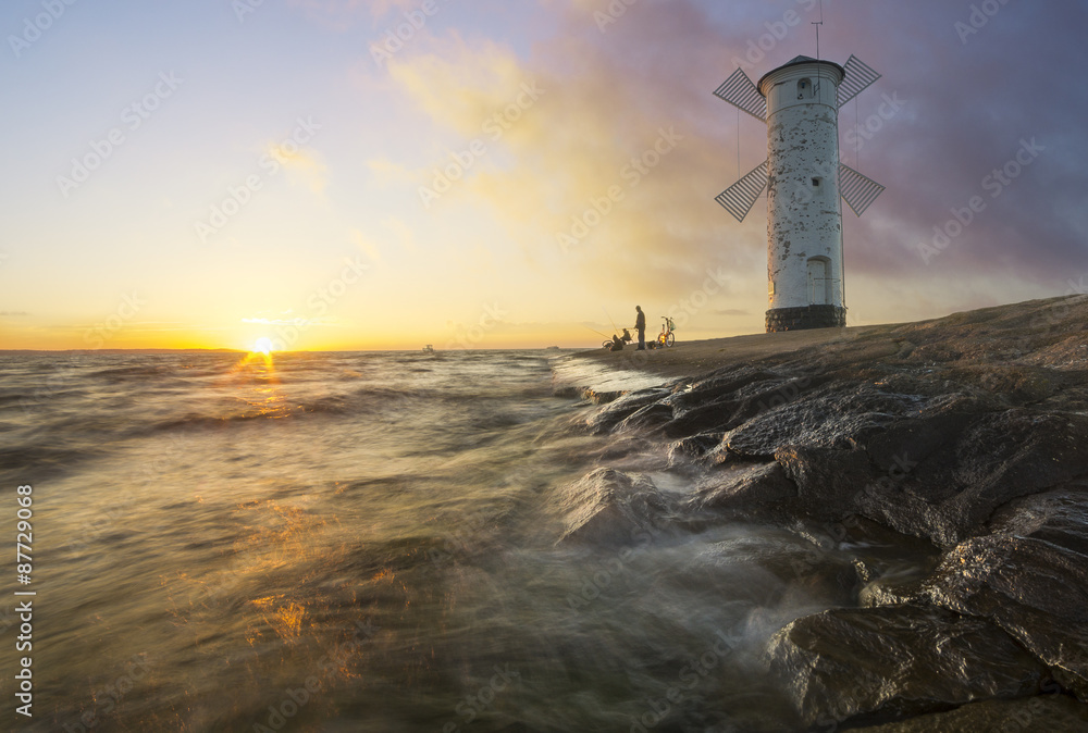 Sunset on the coast, lighthouse windmill in Swinoujscie, Poland. 