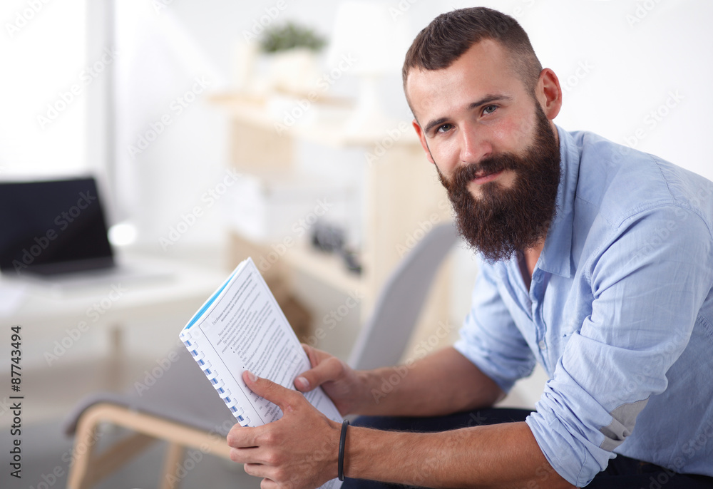 Fototapeta premium Young businessman sitting on chair with book in office