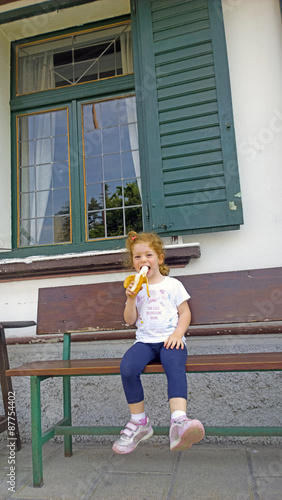 Bambina che mangia banana sorridendo su una panchina