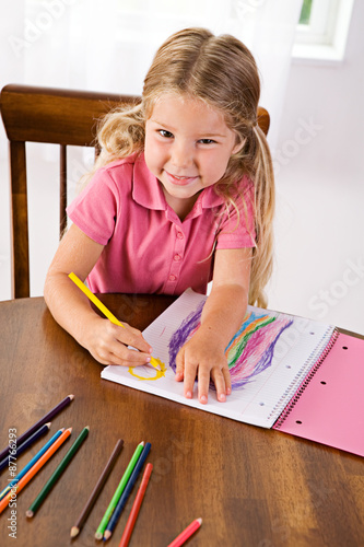 Education: Cute Girl Drawing Rainbow At Table With Colored Penci photo