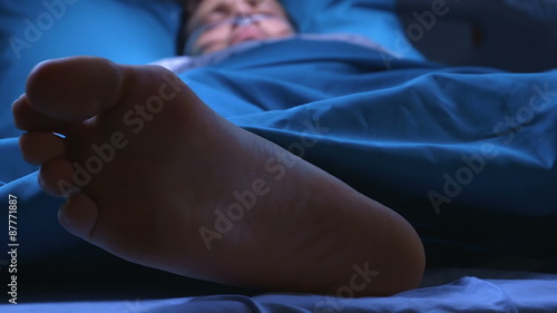 Doctor giving electric shocks with defibrillator to dying man who lies in a hospital bed to try to revive him.