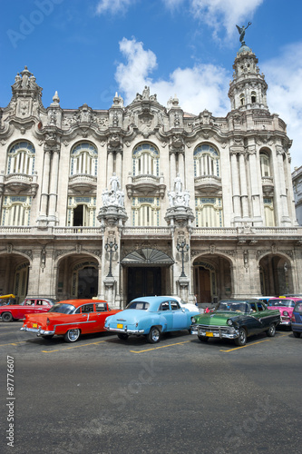 Row of brightly colored vintage American cars stand parked in front of eye-catching colonial architecture © lazyllama