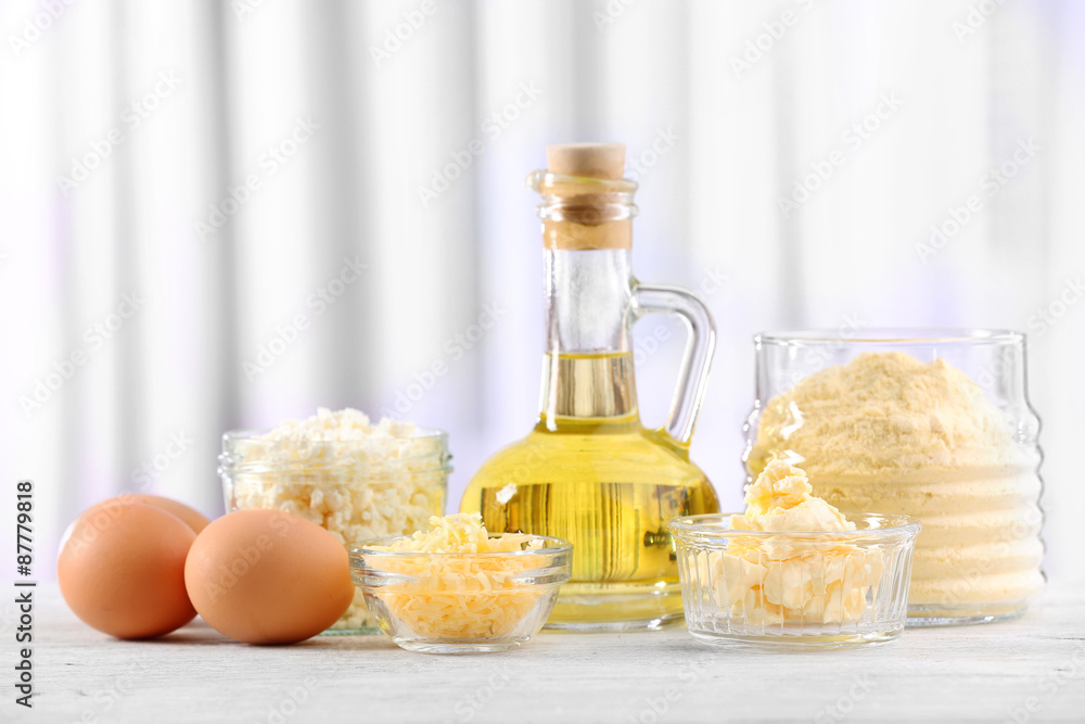 Dairy products, eggs, flour and olive oil in glassware on wooden table on curtain background Dairy products, eggs, flour and olive oil in glassware on wooden table on curtain background
