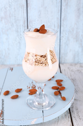 Glass of cream with oatmeal and almonds on color wooden background
