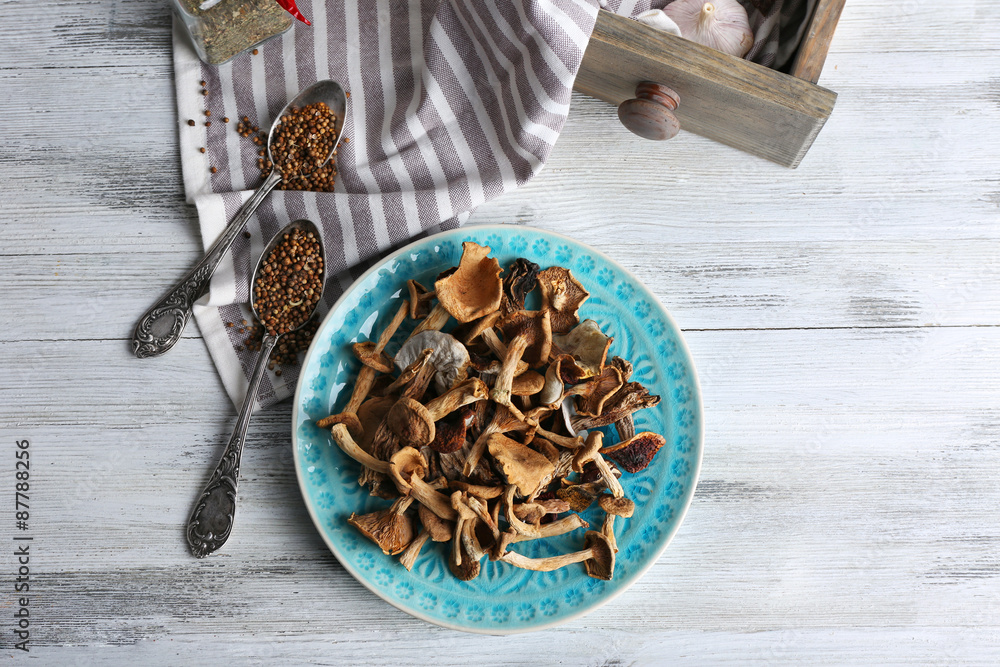 Dried mushrooms in plate with spices on wooden table, top view