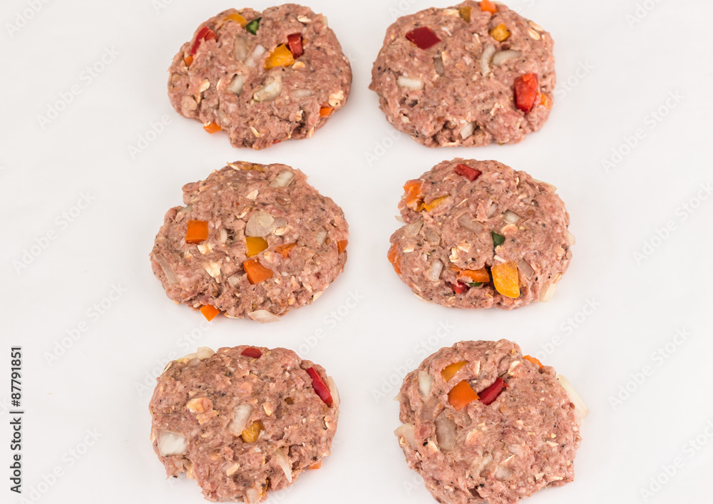 horizontal image of six raw hamburger patties with onion and assorted chopped peppers isolated on white background