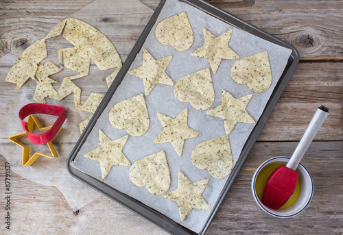 horizontal image of the process of the makings of tortilla chips made into heart and star shapes lying in cookie sheet with some left over tortilla dough and a cookie cutter on rustic wood surface.