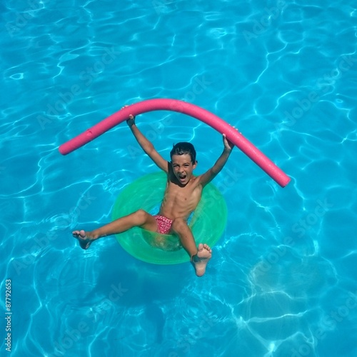 Fototapeta Naklejka Na Ścianę i Meble -  Niño en la piscina con flotador verde