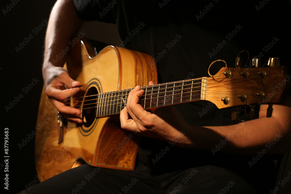 Fototapeta premium Young man playing on acoustic guitar on dark background