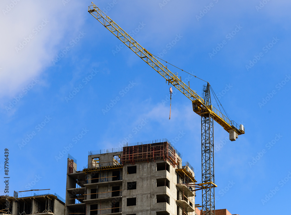 Crane and building construction against blue cloudy sky.