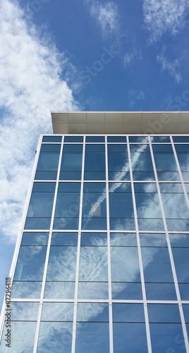 Clouds reflecting in glass windows of modern building, with clouds and sky above