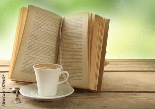 Cup of coffee and book on wooden table, on green background