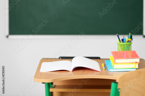 Wooden desk with stationery and chair in class on blackboard background