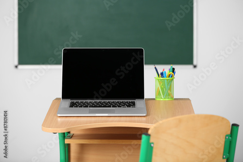 Wooden desk with stationery and laptop in class on blackboard background