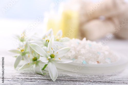 Sea salt, flowers and spa treatment on color wooden table, on light background