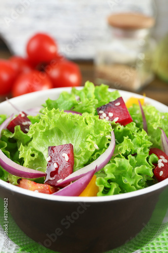 Bowl of fresh green salad on table with napkin, closeup