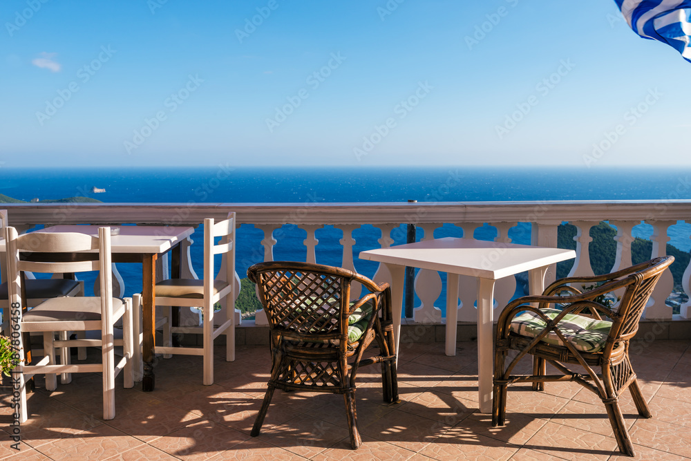 White tables with  chairs and greek flag l in romantic  bay on sunny day, Corfu, Greece