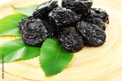 Pile of prunes with leaves on wooden tray, closeup