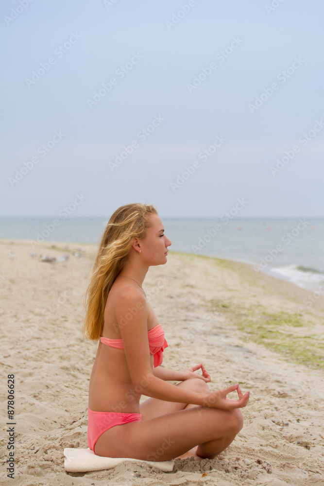 Beautiful girl in bikini sitting and looking at the sea. Yoga and meeting the dawn. Tranquility and meditation.