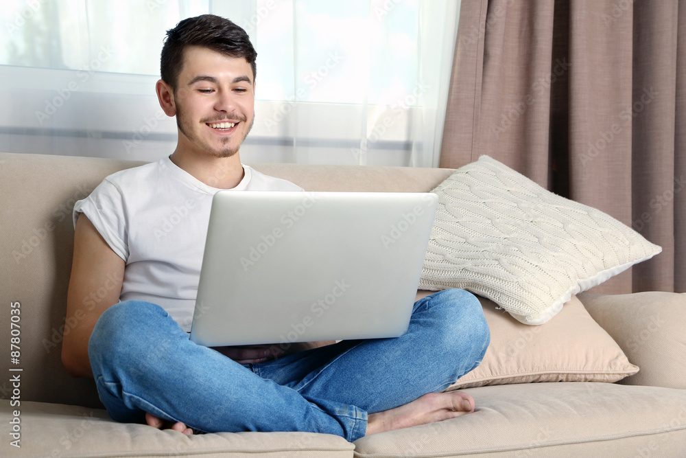 Handsome young man sitting on sofa and using laptop in room Handsome young man sitting on sofa and using laptop in room