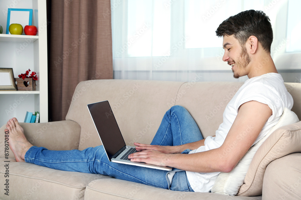 Handsome young man sitting on sofa and using laptop in room Handsome young man sitting on sofa and using laptop in room