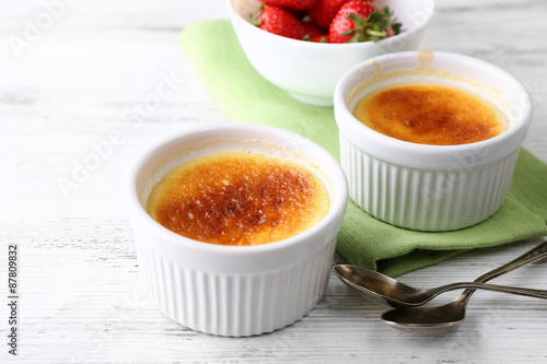 Creme brulee dessert with fresh strawberry berries on napkin, on color wooden background