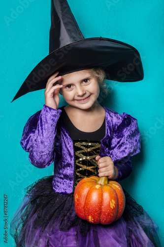 Portrait of little girl in black hat and witch clothing with pumpkin