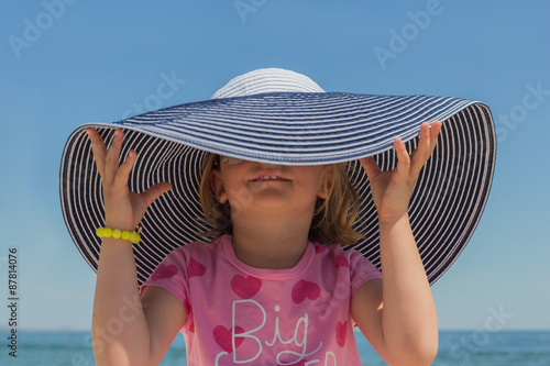 Funny little girl in a big striped hat on the beach.