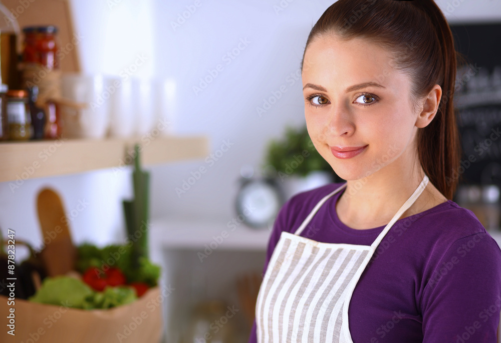 Young woman standing in her kitchen near desk with shopping bags Young woman standing in her kitchen near desk with shopping bags