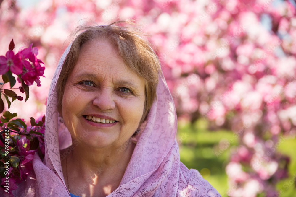 Fototapeta premium Happy adult woman in kerchief under purple flowers in garden