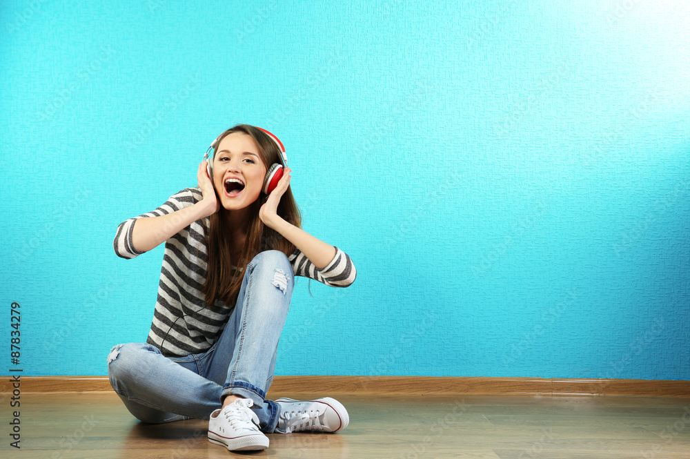 Young woman sitting on floor with headphones on turquoise wallpaper background Young woman sitting on floor with headphones on turquoise wallpaper background