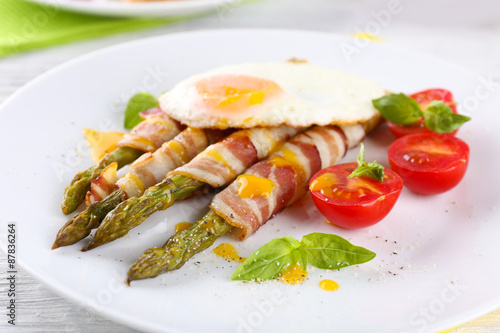 Dish of asparagus with bacon and egg in plate on table  closeup