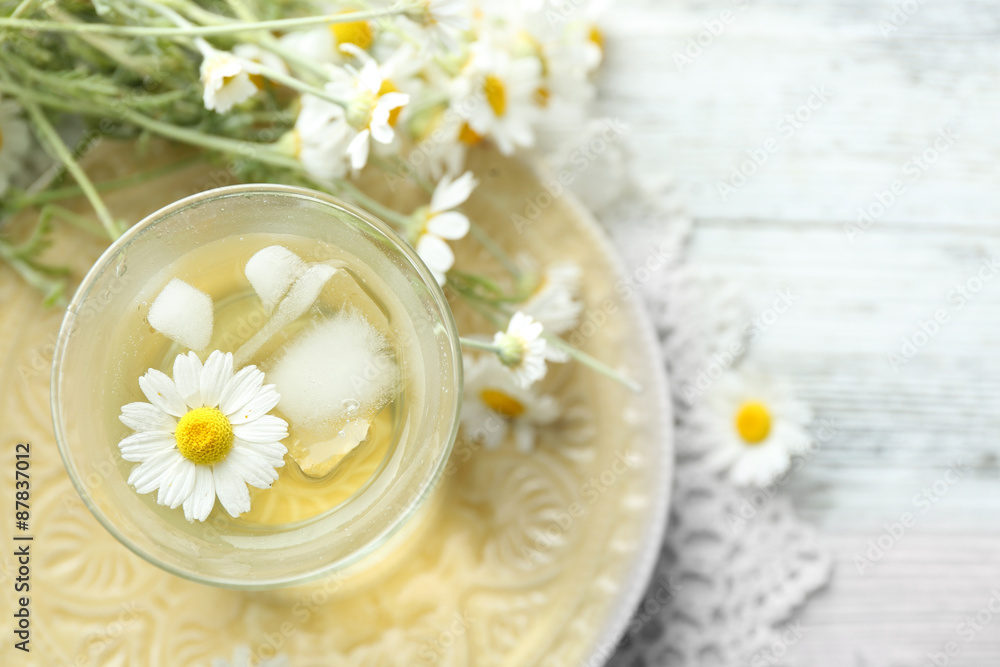 Glass of cold chamomile tea with ice cubes and chamomile flowers on color wooden background Glass of cold chamomile tea with ice cubes and chamomile flowers on color wooden background