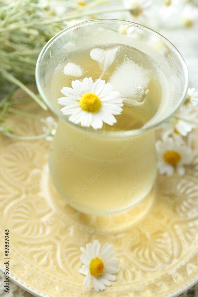 Glass of cold chamomile tea with ice cubes and chamomile flowers on color wooden background Glass of cold chamomile tea with ice cubes and chamomile flowers on color wooden background