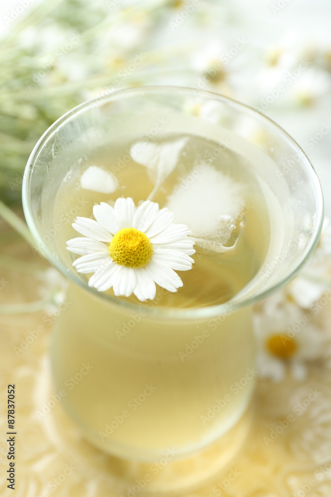 Glass of cold chamomile tea with ice cubes and chamomile flowers on color wooden background Glass of cold chamomile tea with ice cubes and chamomile flowers on color wooden background