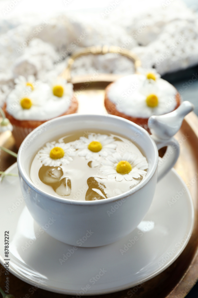 Cup of chamomile tea with chamomile flowers and tasty muffins on tray, on color wooden background Cup of chamomile tea with chamomile flowers and tasty muffins on tray, on color wooden background