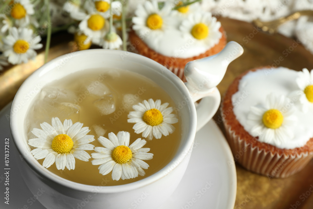 Cup of chamomile tea with chamomile flowers and tasty muffins on tray, on color wooden background