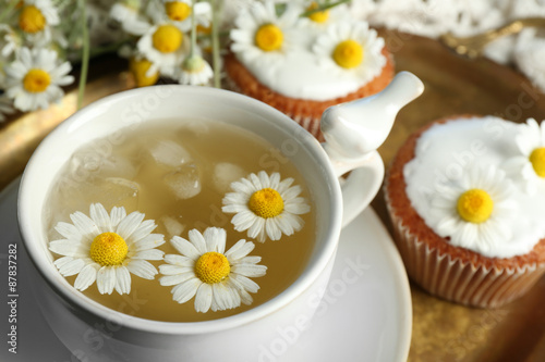 Cup of chamomile tea with chamomile flowers and tasty muffins on tray  on color wooden background