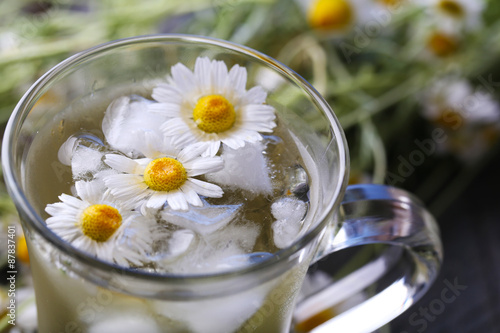 Glass of cold chamomile tea with ice cubes and chamomile flowers on color wooden background © Africa Studio