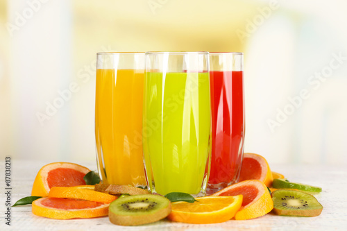 Glasses of different juice with fruits and mint on bright background