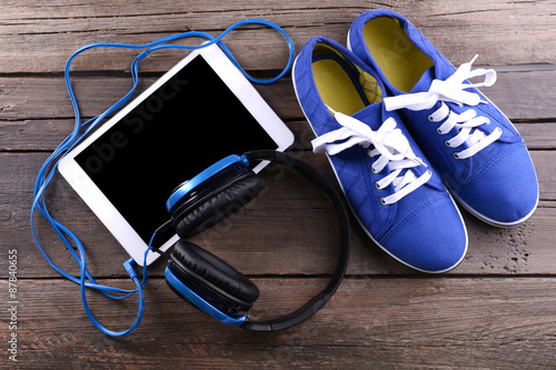 Headphones with sneakers and tablet on wooden background