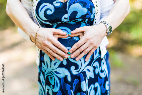 Pregnant Woman and Her Husband holding her hands in a heart 