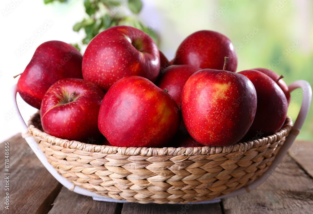 Red apple in wicker basket on wooden table on blurred background Red apple in wicker basket on wooden table on blurred background