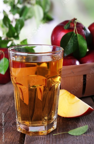 Glass of apple juice with red apples on wooden table on blurred background