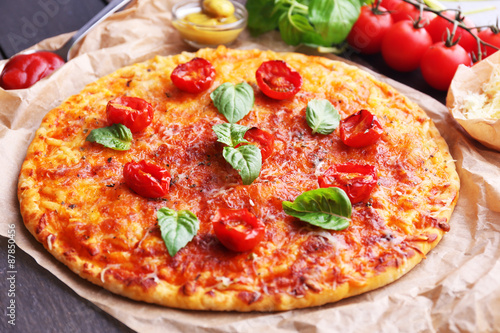 Pizza with basil and cherry tomatoes on parchment, closeup
