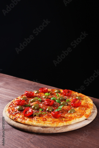 Tasty pizza with cherry tomatoes, green olives and herbs on wooden table on black background