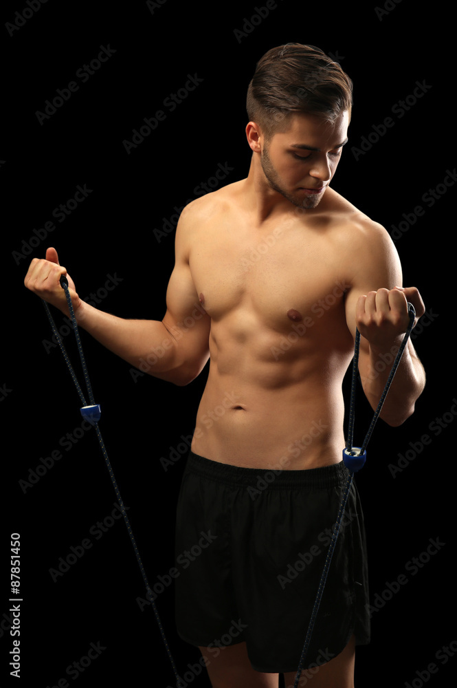 Muscle young man exercising with resistance band on dark background Muscle young man exercising with resistance band on dark background