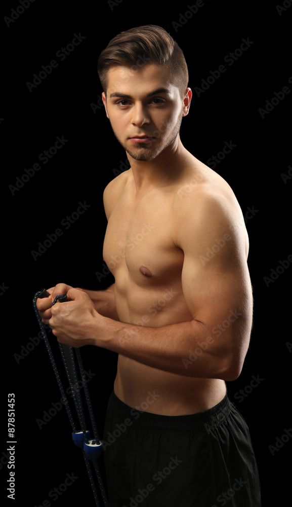 Muscle young man exercising with resistance band on dark background Muscle young man exercising with resistance band on dark background